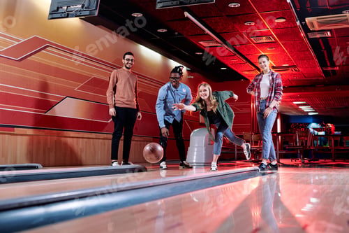Preview: Pretty young female throwing bowling ball on track during play with friends