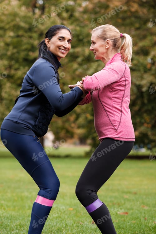 Preview: Two happy mature women using resistance bands in a park.