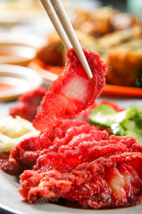 Preview: Piece of red glutinous rice pork being held by chopsticks with a blurred background.
