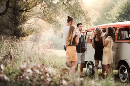 Preview: A group of friends standing outdoors on a roadtrip through countryside, drinking.