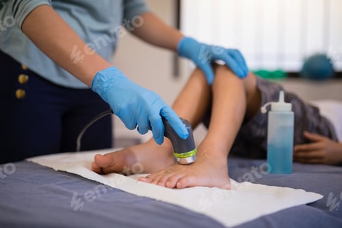 Vista previa: Female therapist wearing gloves scanning feet of boy lying on bed