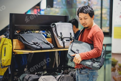 Preview: Smart man with beard trying bag and making decision in fashion bags shop at shopping mall,