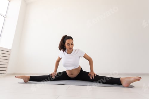 Preview: Purposeful pregnant woman exercises during yoga class and relaxes while sitting on a mat on the
