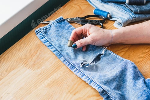 Preview: A woman is repairing ripped blue jeans. The concept of economical reuse of things