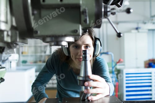 Preview: Woman in workshop wearing ear defenders operating machine smiling