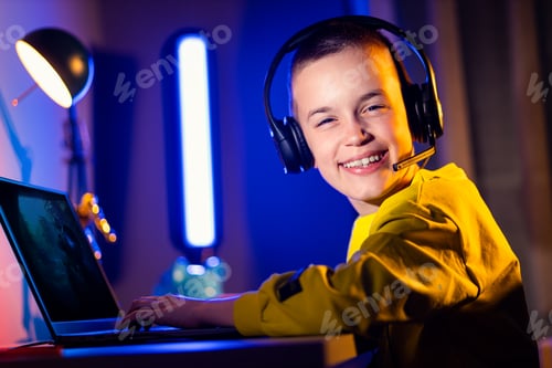 Preview: Young excited boy gamer with headphone playing video game on laptop at home.