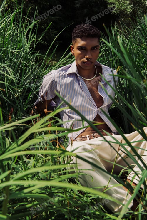 Preview: african american man in blue shirt and beads looking at camera on green grass