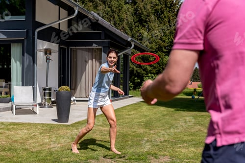 Preview: Happy couple playing with flying disc in garden of their home