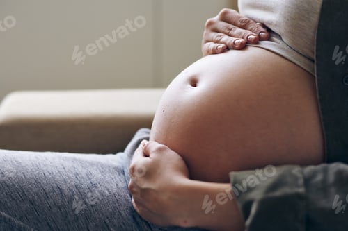 Preview: Hands of young woman in cotton casualwear on her pregnant belly