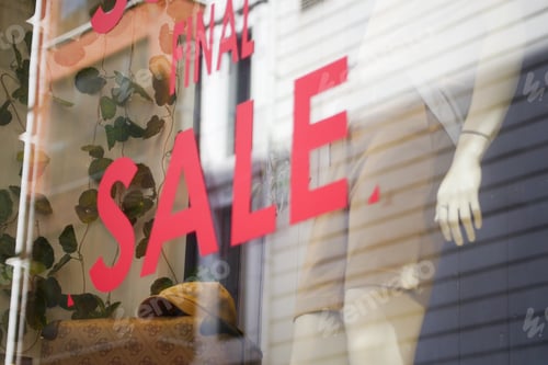 Preview: Red Sale Sign in Clothing Store Featuring Large Bold Text on Promotional Board