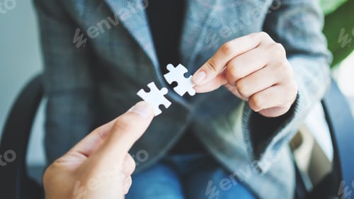 Preview: Closeup image of two businesswoman holding and putting a piece of white jigsaw puzzle together