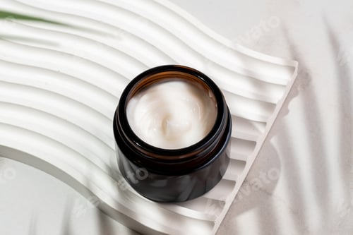 Preview: Dark glass cosmetic jar with a collagen cream on marble background with tropical leaf shadow. Nature