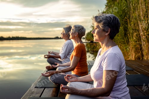 Preview: Group of senior woman doing yoga exercises by the lake.