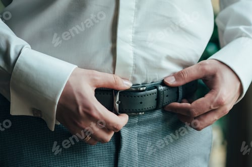 Preview: A man in blue pants and a white shirt buttoned a brown leather trouser belt