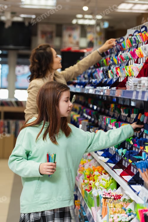 Preview: girl with new pens choosing school supplies near blurred mom in stationery store