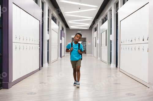 Preview: Full length of african american elementary schoolboy with backpack walking in school corridor