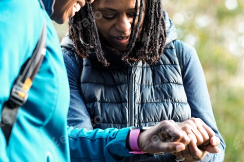 Preview: Two female mature friends monitoring their smart watches outdoors.