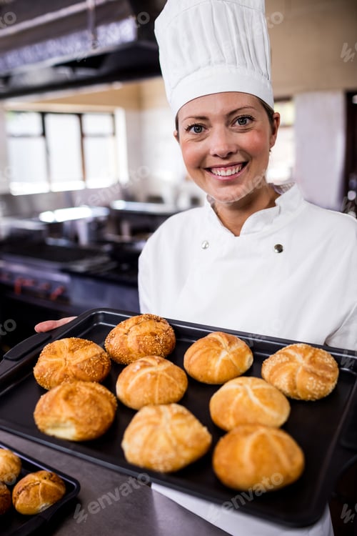 Preview: Female chefs holding baking tray of kaiser rolls in kitchen