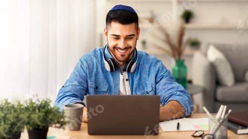 Preview: Smiling israeli man working on laptop at home