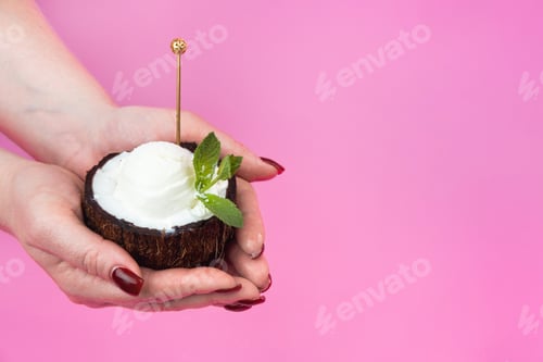 Preview: Vanilla ice cream balls in a fresh coconut half, decorated with mint leaves in the hand with a spoon