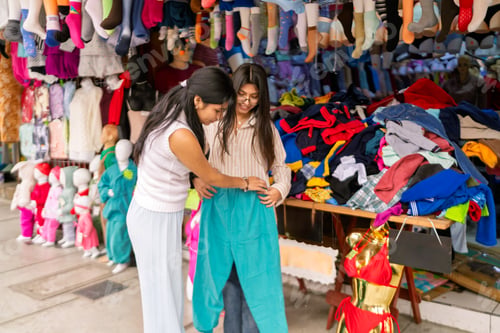 Preview: Two women friends shopping trying on clothes at market