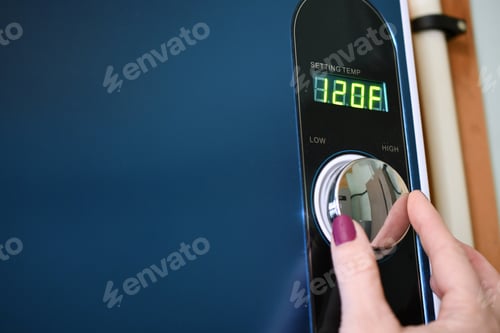Preview: Female hand adjusting a tankless instant hot water heater. Energy efficient efficiency, conservation