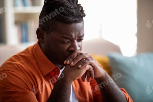 Preview: Depressed black guy sitting alone on couch at home, closeup
