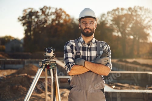 Preview: Standing by the geodetic optical level. Worker is on the construction site at daytime