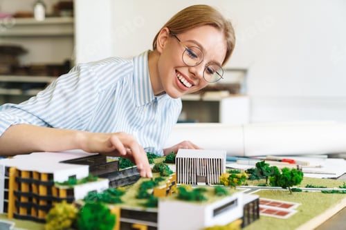 Preview: Photo of joyful young woman architect designing draft with house model