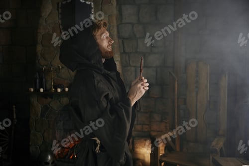 Preview: Faithful priest in robe hood praying with rosary beads and cross