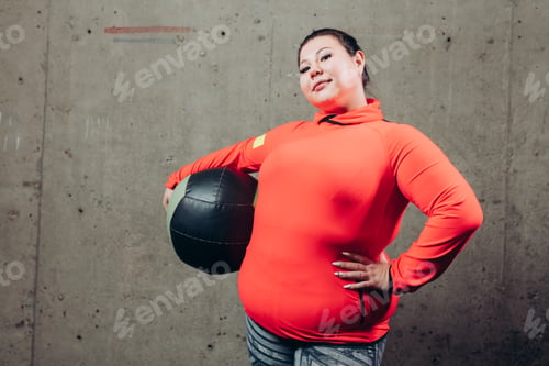 Preview: pleasant overweight woman with exercise ball isolated on gray background