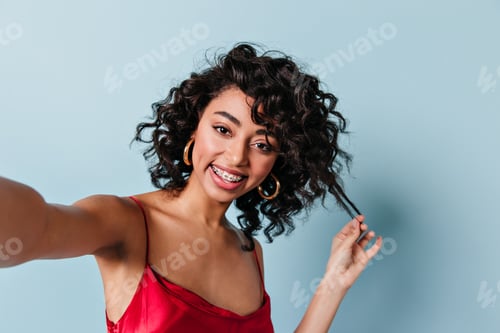 Preview: Stunning mixed race lady taking selfie. Studio shot of laughing curly girl posing on blue backgroun