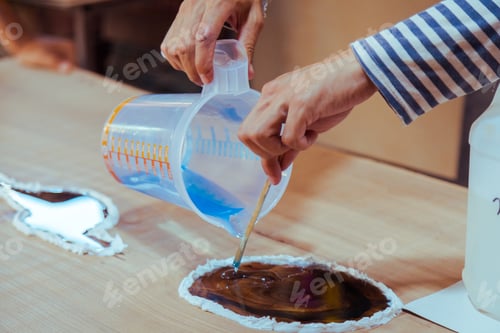 Preview: Closeup of carpenter pouring liquid epoxy in a wooden table