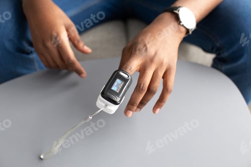 Preview: Man with pulse oximeter on hand measuring oxygen saturation indoor