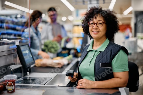 Preview: Happy woman working as cashier at supermarket checkout and looking at camera.
