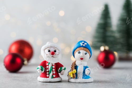 Preview: Figurines of Santa Claus and Snow Maiden against a background of Christmas balls and bokeh.