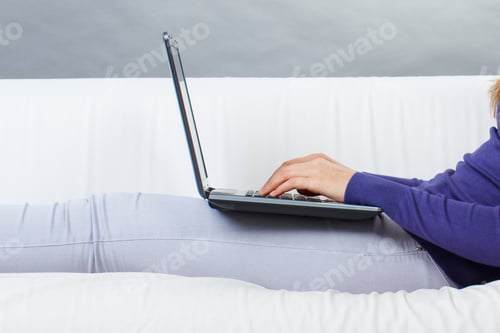 Preview: Woman working on laptop while relaxing on couch