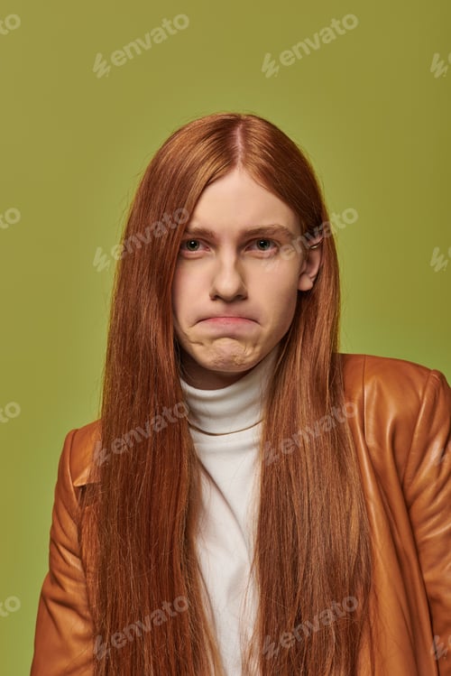 Preview: Emotion reflected on a young mans face with long red hair in a vibrant green setting