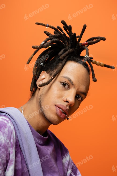 Preview: portrait of fashionable multiracial man with piercing and dreadlocks looking at camera isolated on