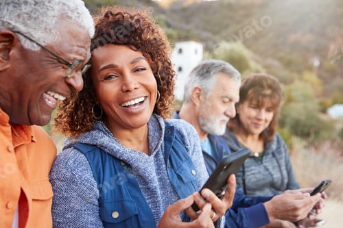 Preview: Group Of Senior Friends On Hike In Countryside Looking At Mobiles Phones Together