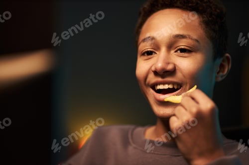 Preview: Portrait of Smiling Multiethnic Teenager Boy Eating Potato Chips Indoors