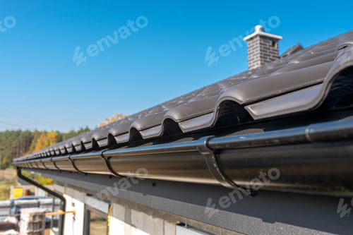 Preview: A metal, black gutter on a roof covered with ceramic tiles. Close up shot.