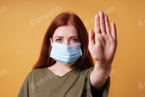 Preview: young woman wearing medical face mask making stop gesture with her hand. no entry without mask