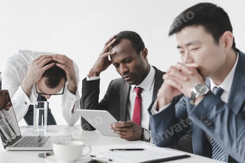 Preview: multicultural tired businessmen using tablet together during meeting at workplace