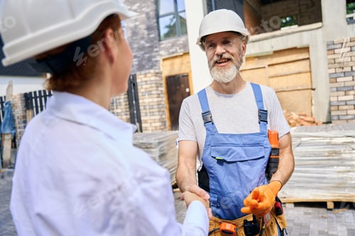 Preview: Friendly building contractor greeting site manager with handshake outdoors