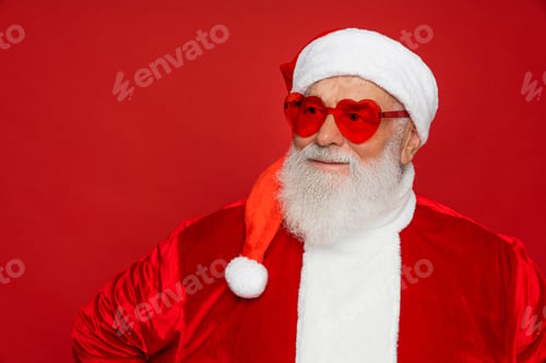 Preview: Funny Santa Claus wearing sunglasses looking aside away on copy space isolated on red background.