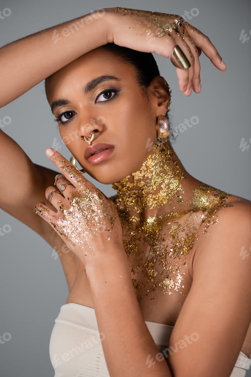 Preview: Trendy african american woman with accessories and golden foil on body and hands posing isolated