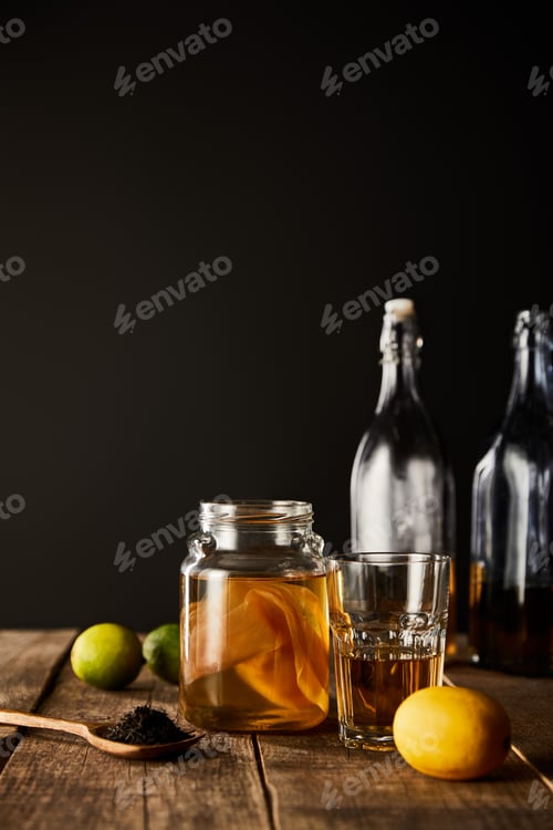 Preview: glass jar with kombucha near lime, lemon, spice and bottles on wooden table isolated on black