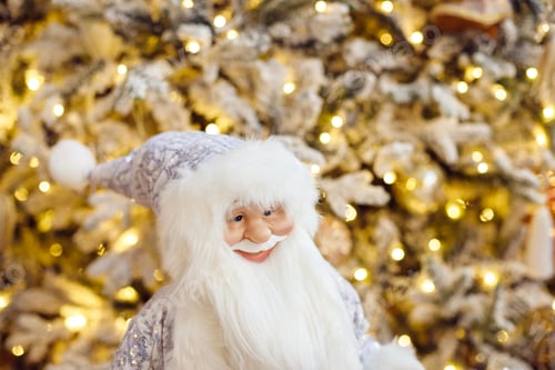 Preview: A toy of santa claus in a white suit stands on in living room near christmas tree. Christmas tree