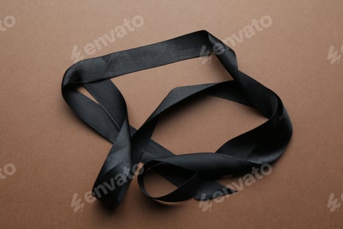 Preview: Beautiful black ribbon on light brown background, top view